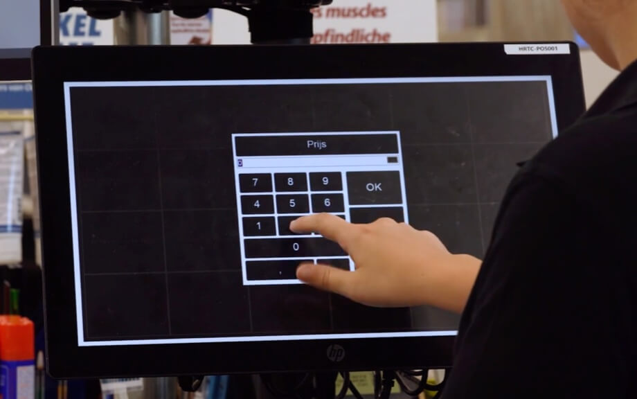 Een kassier tikt de prijs in op een touchscreen aan de kassa.