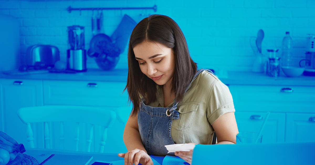 Een vrouw die aan haar keukentafel een lijst maakt van haar webshop kosten.